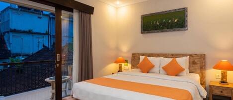 Habitación de hotel con una cama grande, dos lámparas de noche, un cuadro en la pared y un balcón con vistas a edificios.