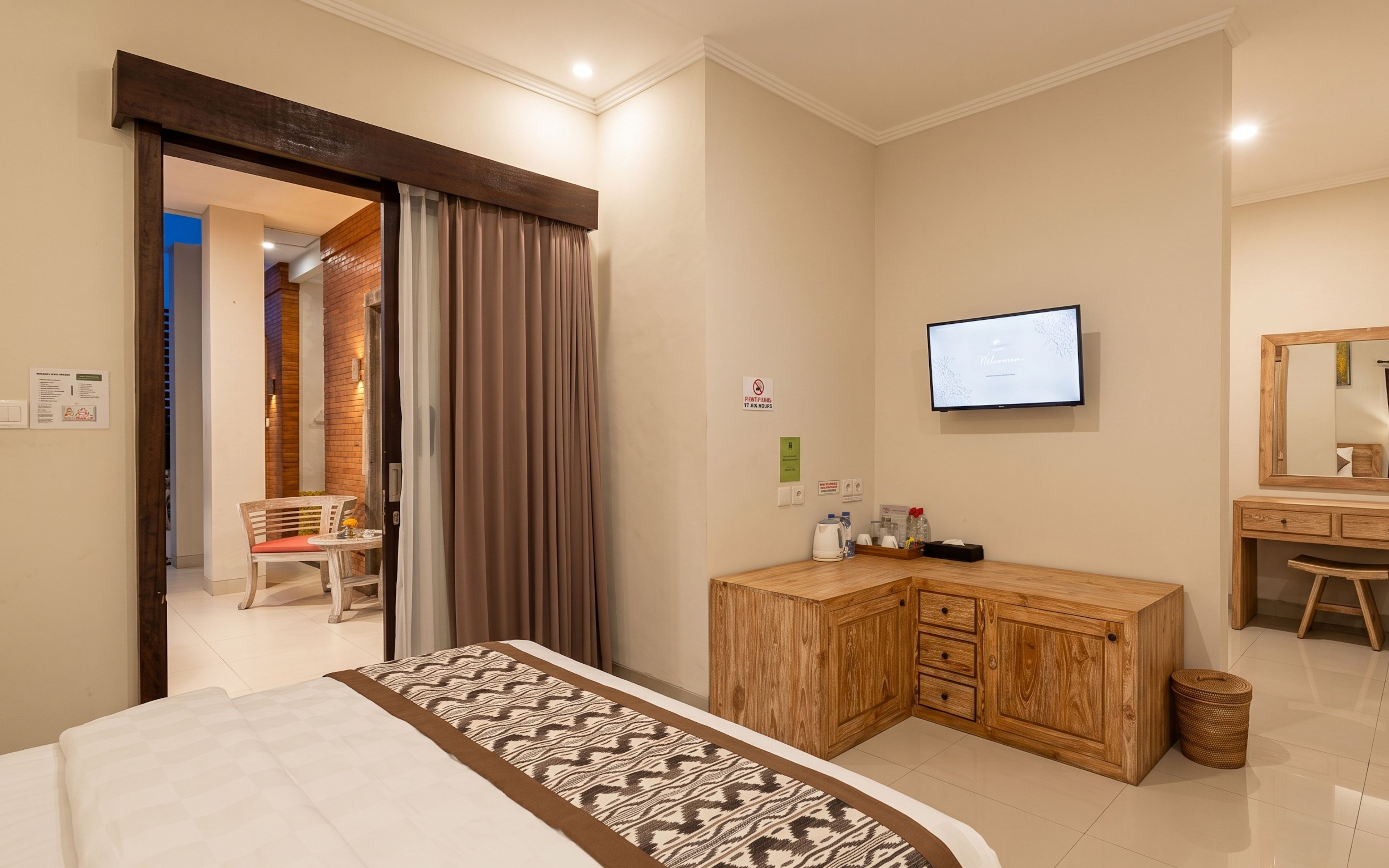 Quarto de hotel com uma cama, escrivaninha de madeira, televisão e espelho.