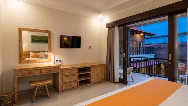 Habitación de hotel con cama, escritorio con silla, televisión y balcón con vista al exterior.