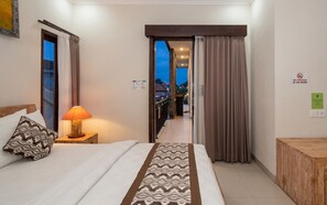 A hotel room with a bed, a nightstand with a lamp, a patterned throw, a view through an open door, and a 'No Smoking' sign. - Rumah Kultur (Ubud)