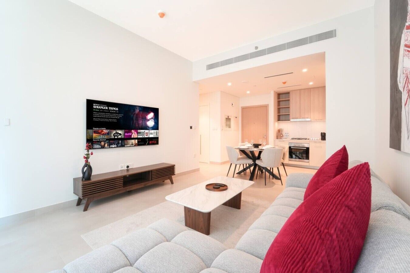 A modern living room with a flat-screen TV, a sofa, a coffee table, and a dining area with a table and chairs.