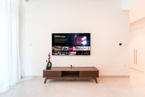 A modern living room with a flat-screen TV mounted on the wall, a wooden console table, and a vase with flowers. - Modern 1BR Retreat in Parkside Views | Dubai Hills (Dubai)