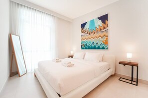 Une chambre d’hôtel avec un grand lit, un tableau au mur, une table de chevet avec une lampe et une fenêtre avec des rideaux.