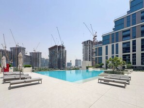 A rooftop swimming pool with lounge chairs and umbrellas, surrounded by high-rise buildings under construction. - Modern 1BR Retreat in Parkside Views | Dubai Hills (Dubai)