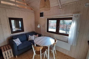 A room with a wooden interior, a round table with chairs, a sofa with cushions, and a window with curtains.
