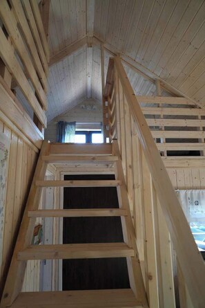 Una escalera de madera que sube a un altillo con techo inclinado y una ventana en la parte superior.