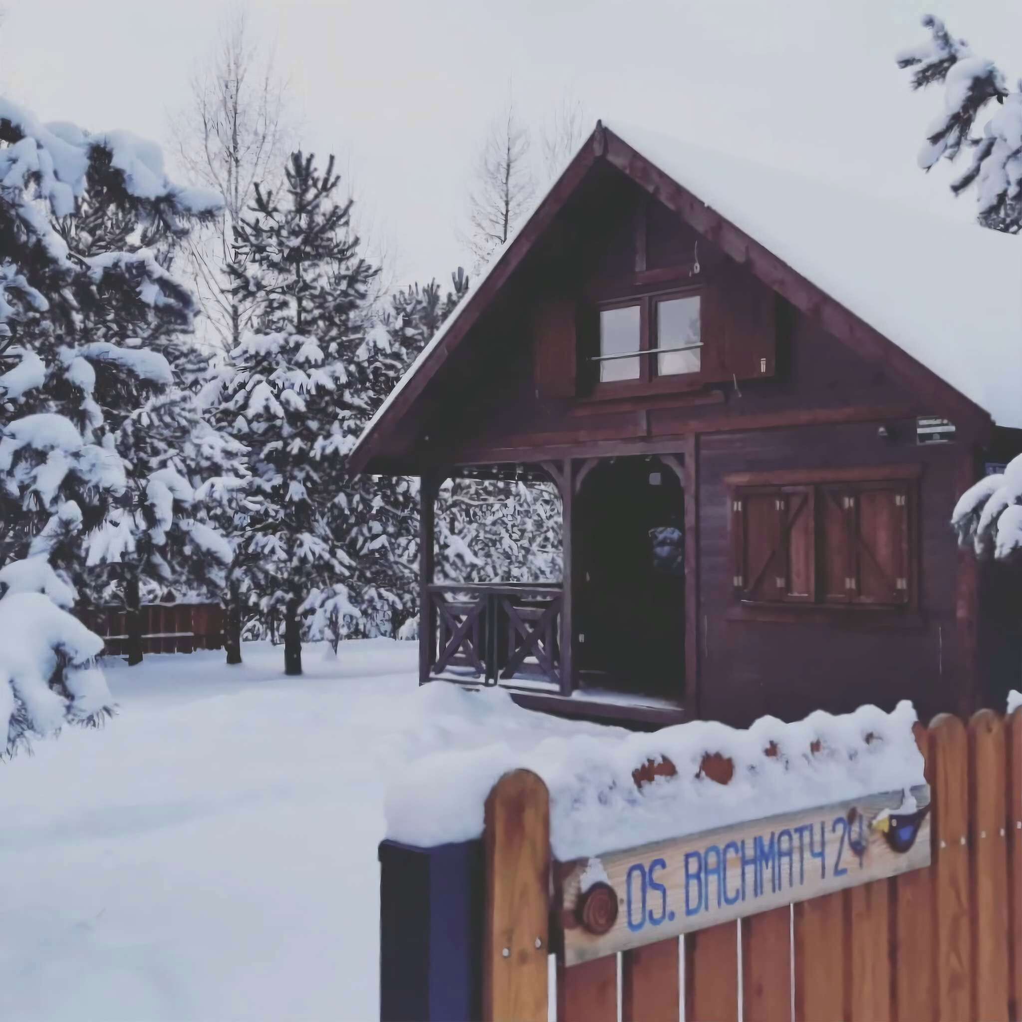 A wooden cabin with a porch, surrounded by snow-covered trees.