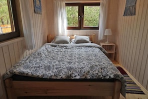 A wooden-paneled bedroom with a bed, two windows, a nightstand, and a lamp. - Nasze Podlasie - Cottage in Dubicze Cerkiewne (Dubicze Cerkiewne)