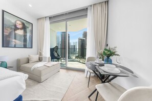 Ein modernes Wohnzimmer mit einer Couch, einem Esstisch für zwei Personen und einem großen Fenster mit Blick auf die Stadt.
