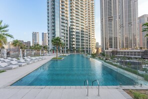 Ein Pool mit Liegestühlen und Palmen, umgeben von Hochhäusern.