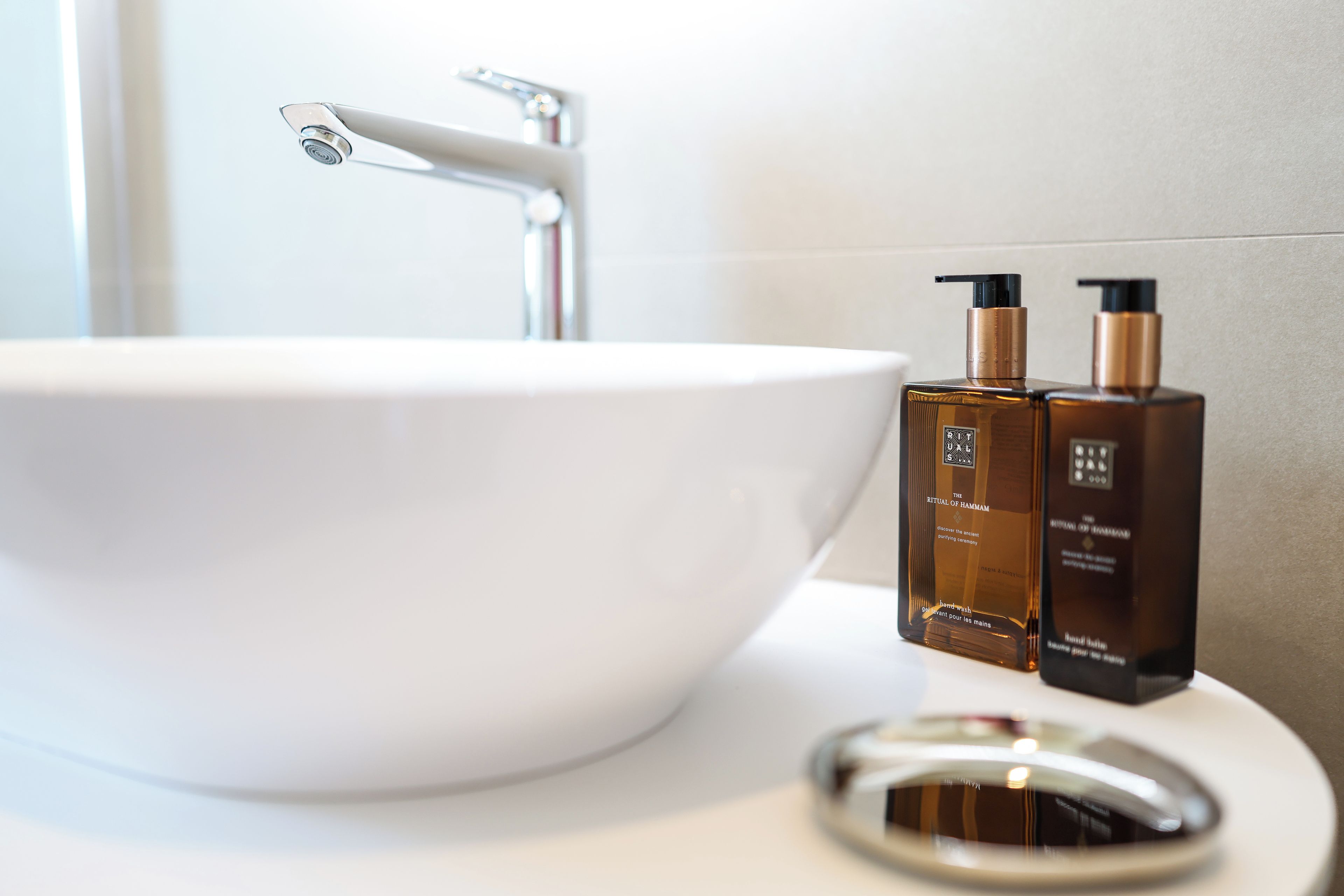 A bathroom with a white sink, two brown bottles, and a modern faucet.