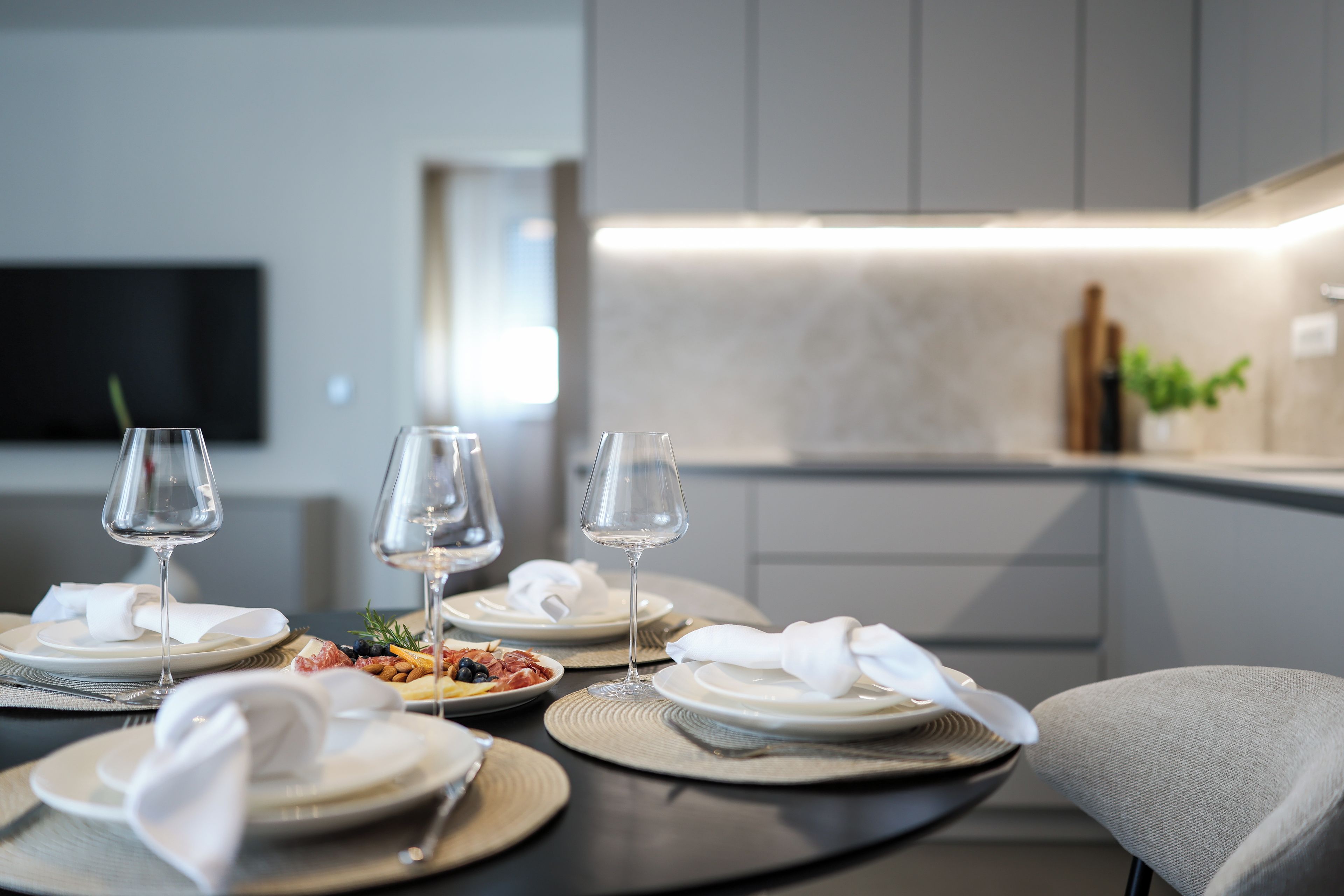 Un espace repas moderne avec une table ronde dressée pour deux personnes, agrémentée d’assiettes blanches, de couverts et de verres.