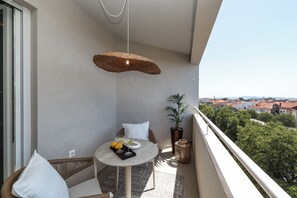 A balcony with a round table, wicker furniture, a hanging light fixture, a potted plant, and a view of a cityscape. - Apex Refined Apartment Antun Zadar (Zadar)