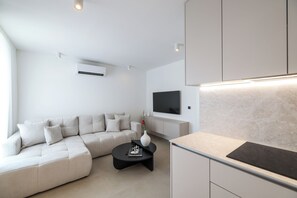 A modern living room with a sectional sofa, a flat-screen TV mounted on the wall, and a kitchen area with a countertop. - Apex Refined Apartment Antun Zadar (Zadar)
