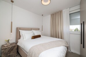 A modern bedroom with a bed, bedside tables, a nightstand, a window with curtains, and a view of the outside. - Apex Refined Apartment Antun Zadar (Zadar)