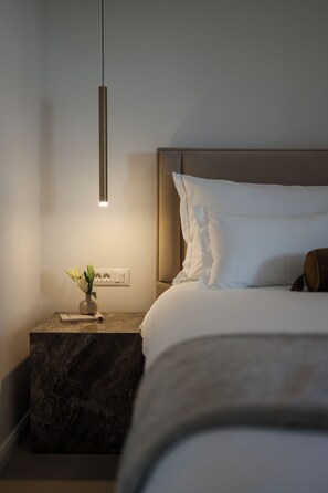 Quarto moderno com cama, mesa de cabeceira e luminária pendente.