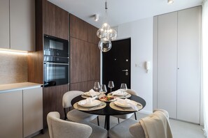 A modern dining area with a round table set for two, a built-in oven, and a black door. - Apex Refined Apartment Antun Zadar (Zadar)