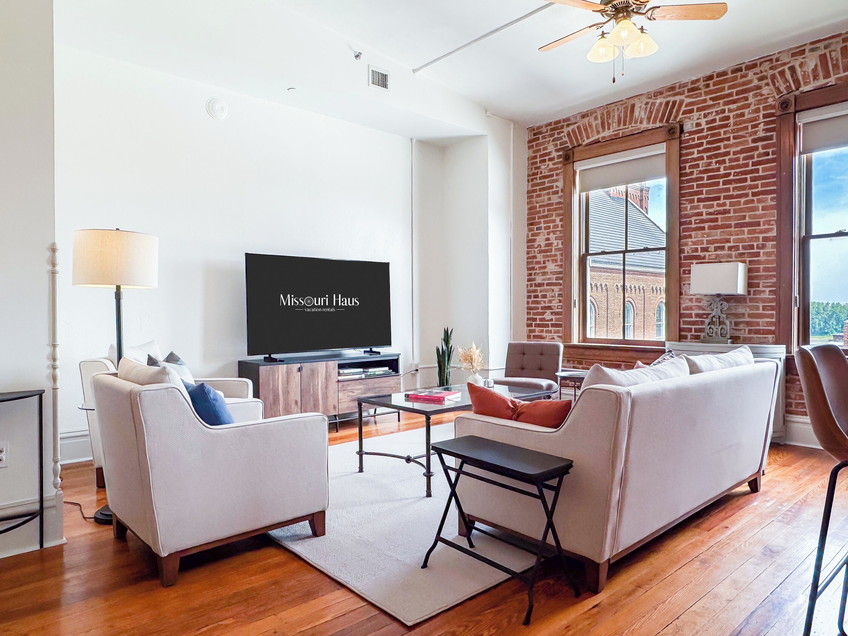 A modern living room with a flat-screen TV, a sofa, a coffee table, and a brick wall.