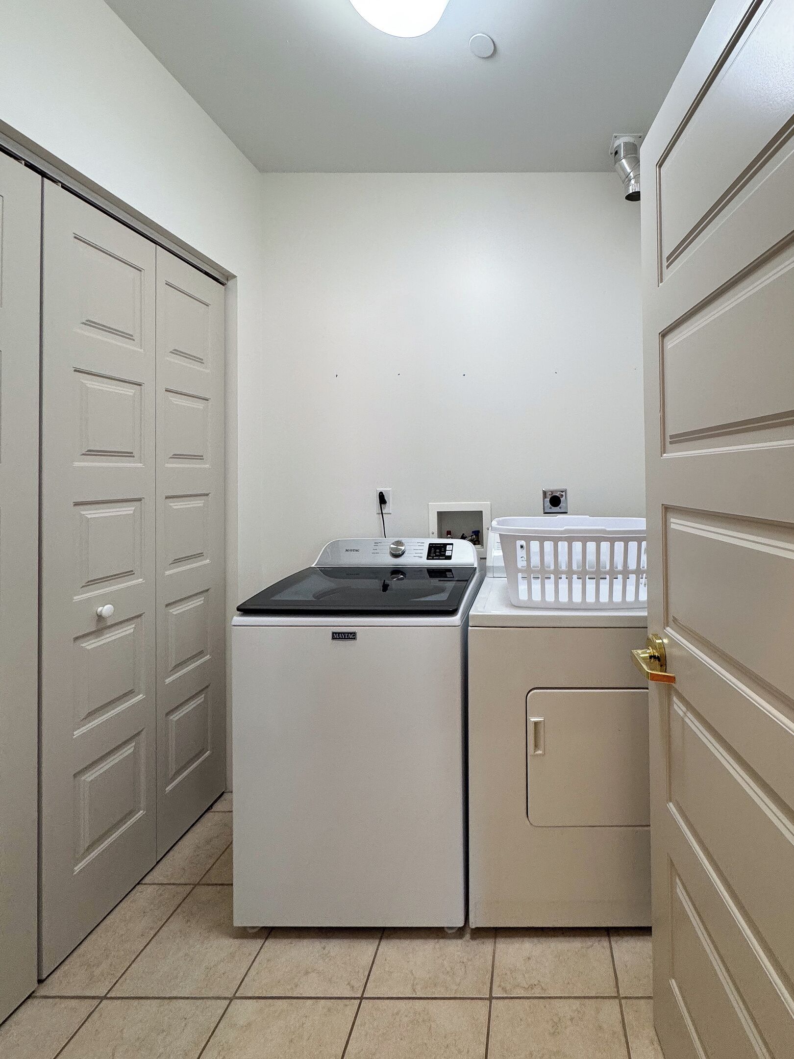 A laundry room with a washer and dryer, a white laundry basket, and a door with a keyhole.