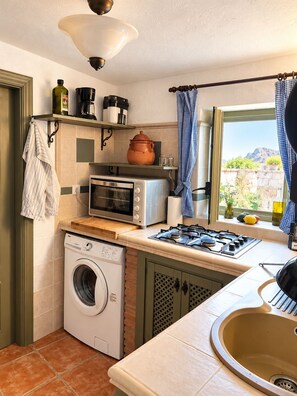 A compact kitchen with a washing machine, microwave, and gas stove. - Welcome to Casa Berberi (Montejaque)