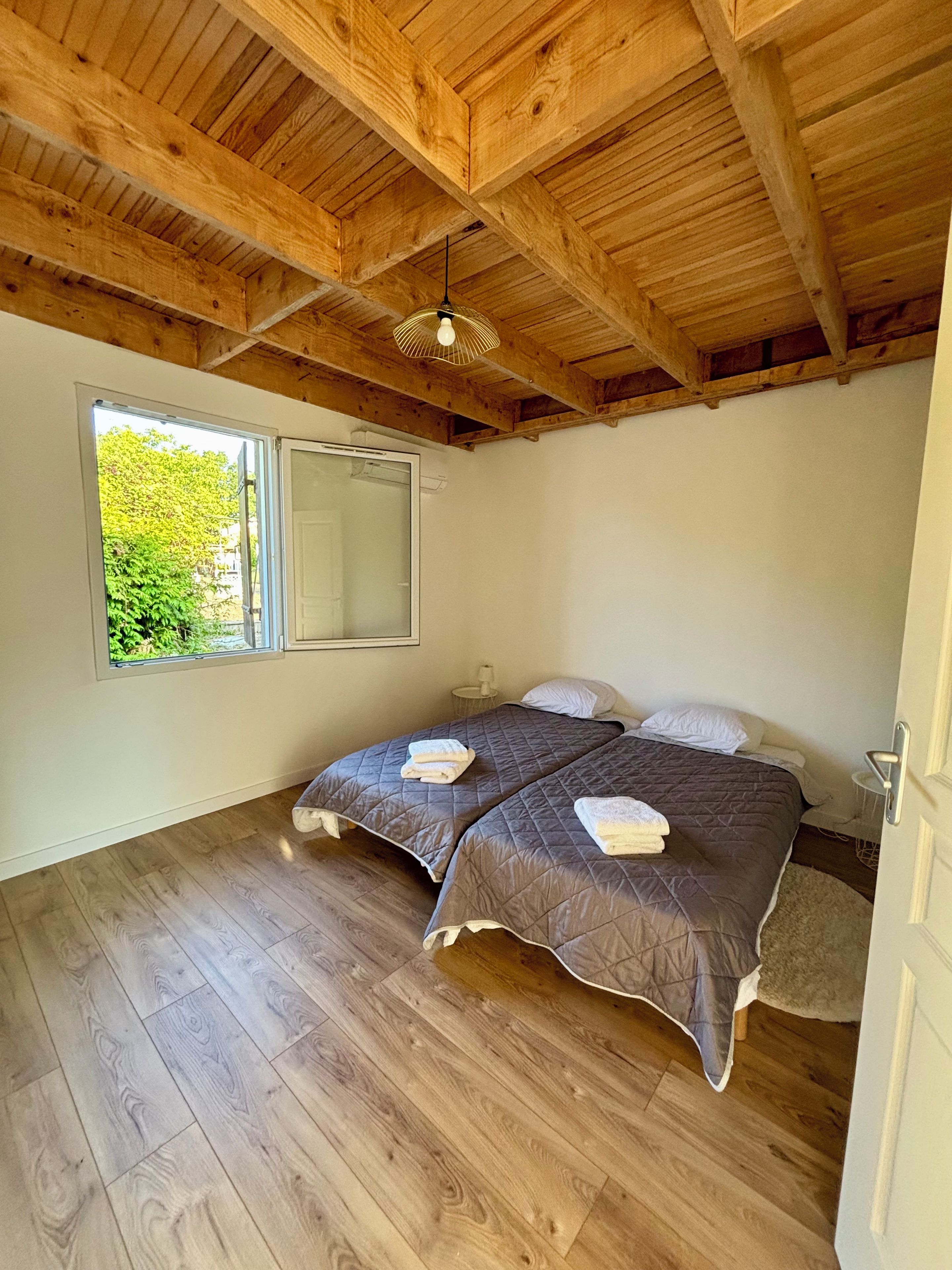 Un dormitorio con dos camas, suelo de madera, un ventanal grande y techo de madera.