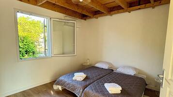 Une chambre avec deux lits, un plancher en bois, une grande fenêtre et un plafond en bois.