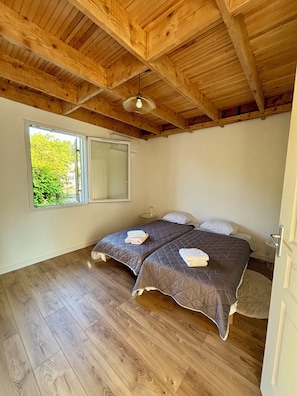 A bedroom with two beds, wooden flooring, a large window, and a wooden ceiling.