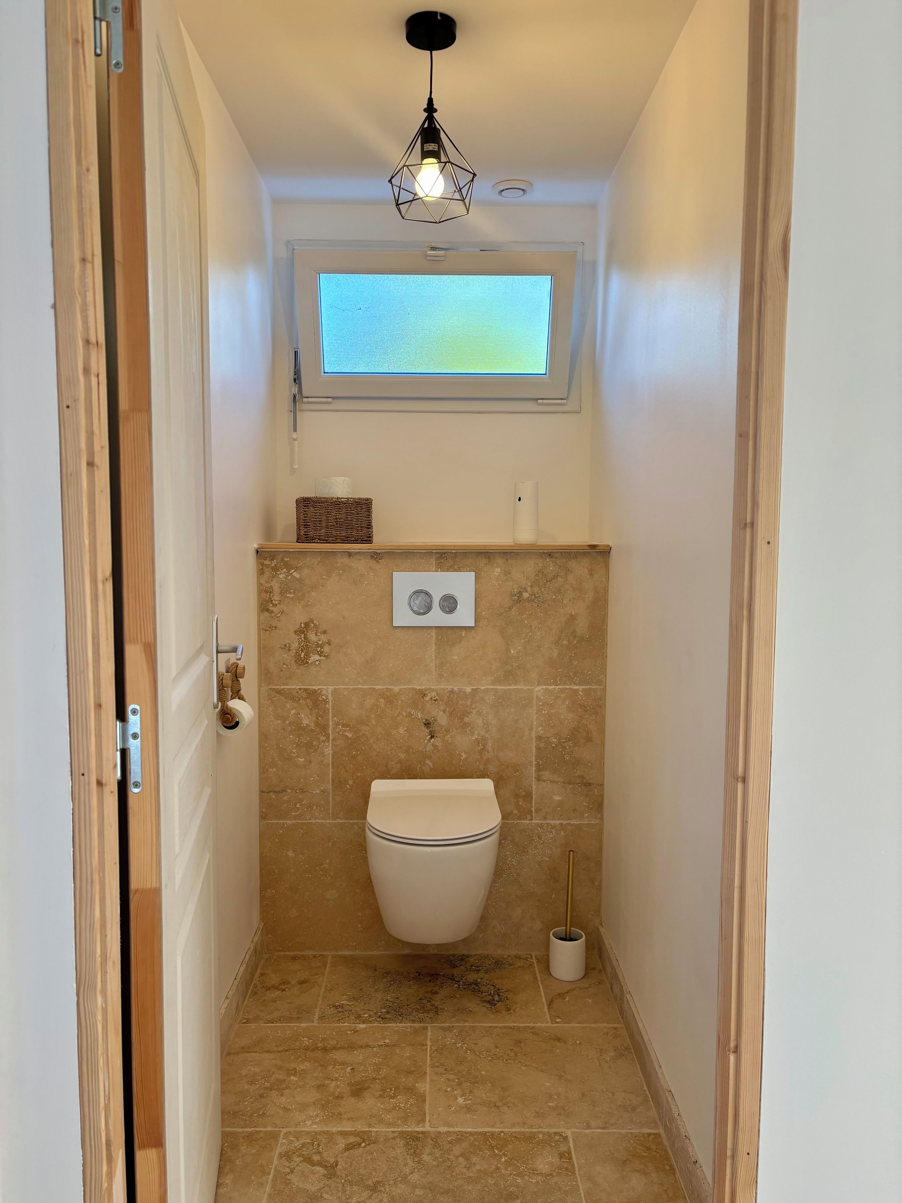 A small bathroom with a toilet, a window, and a light fixture.