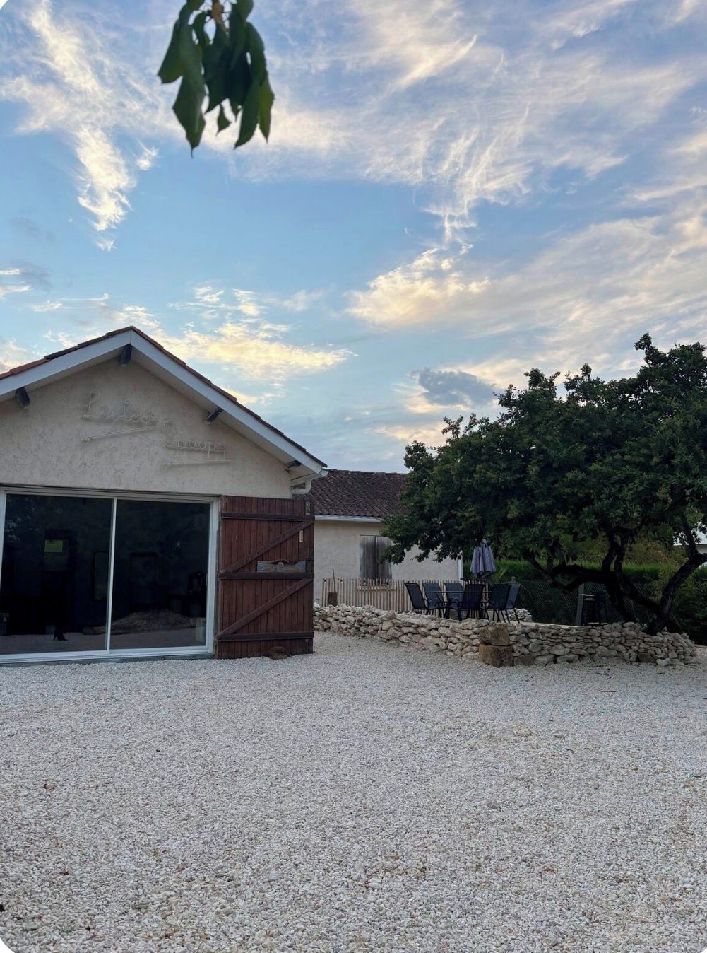 Un bâtiment doté d’un toit en pente, d’une clôture en bois et d’une allée gravillonnée.