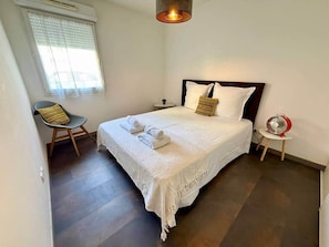 Una camera da letto con un letto, una sedia, un comodino e una ventola.