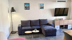 Ett modernt vardagsrum med en hörnsoffa, ett litet runt bord, en platt-TV och ett skrivbord.