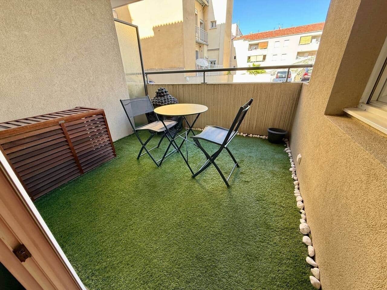 A small outdoor area with artificial grass, a table, two chairs, and a wooden bench.