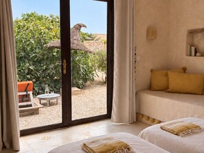 A room with a bed, a small table, and a chair, with a view of greenery outside. - Palais Amani (Aït Chouer)