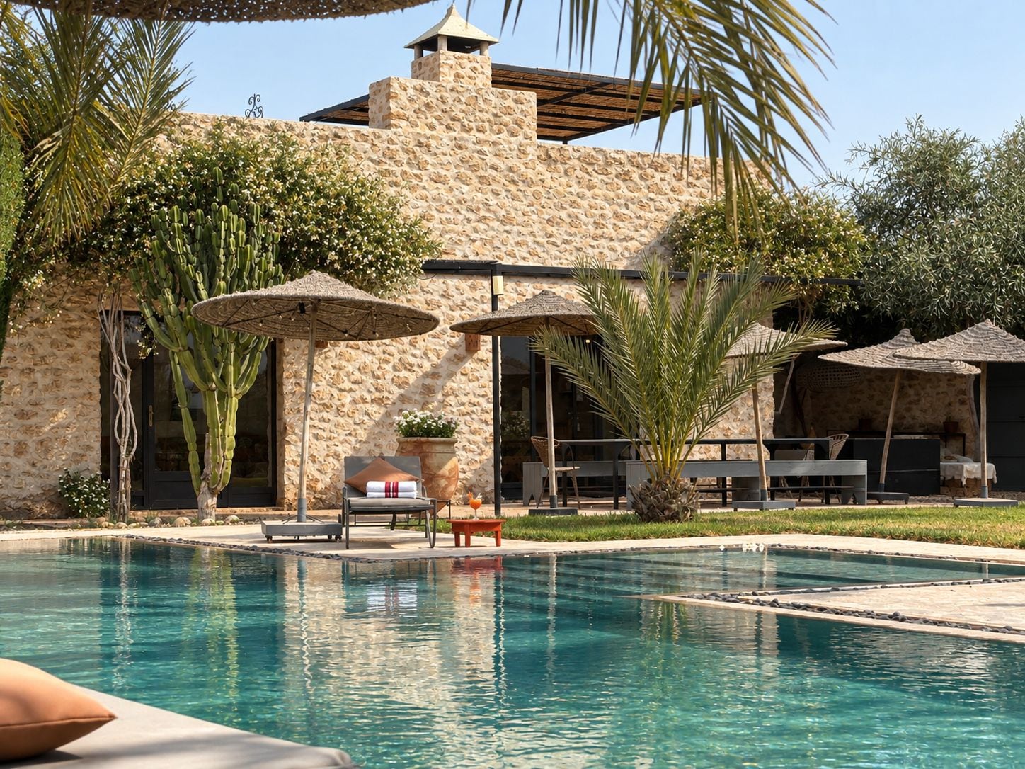 Un área de piscina con un edificio de piedra, sombrillas y mobiliario exterior.