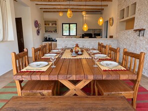 A dining area with a wooden table set for a meal, surrounded by chairs, with hanging pendant lights above. - Palais Amani (Aït Chouer)