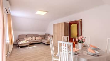 A modern living room with a sofa, dining table, and chairs. There is a wooden cabinet and a decorative mirror.