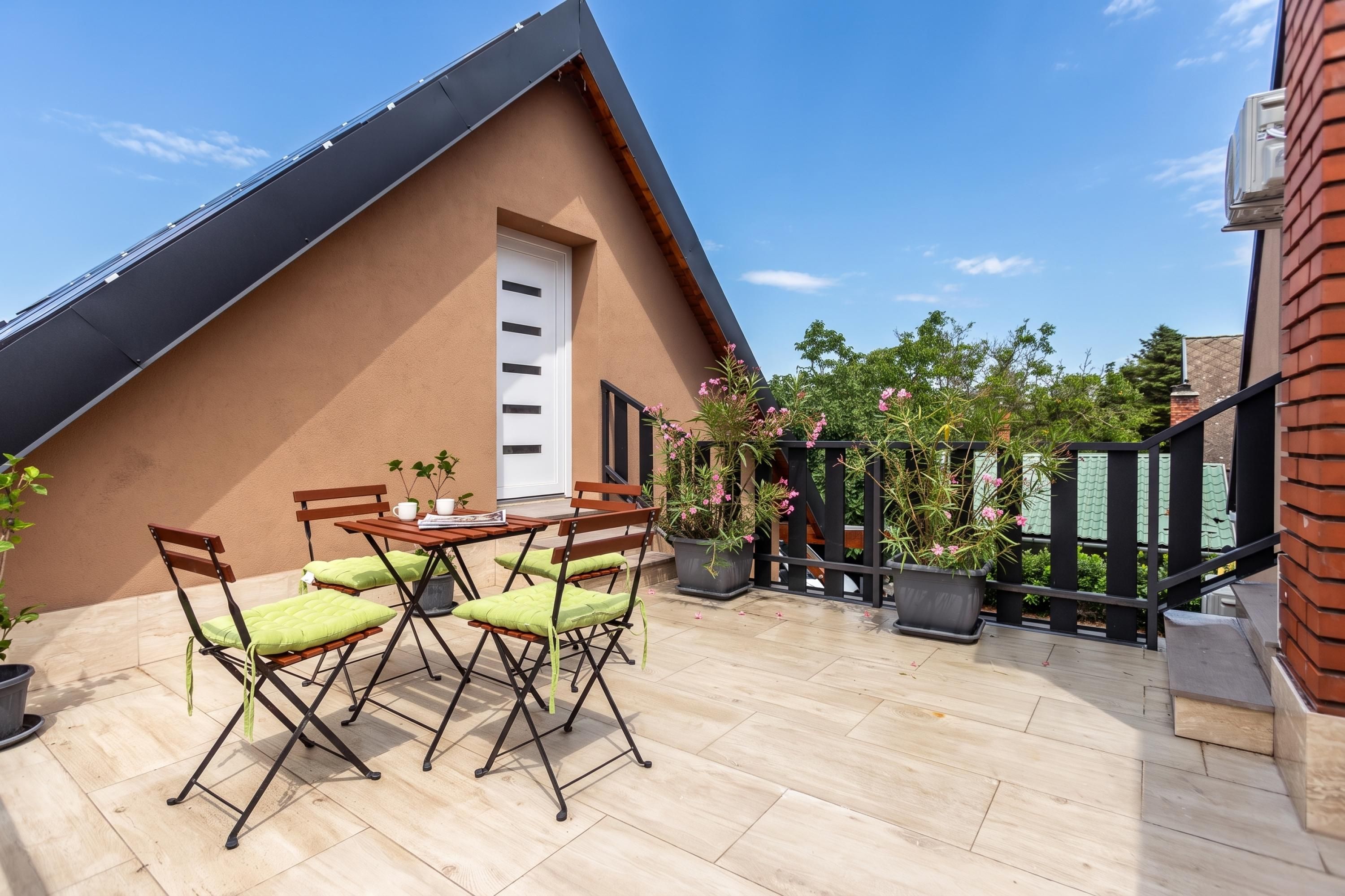 A rooftop terrace with a table and chairs, potted plants, and a view of the surrounding area.
