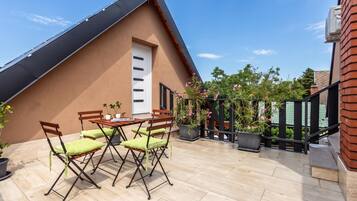 A rooftop terrace with a table and chairs, potted plants, and a view of the surrounding area.
