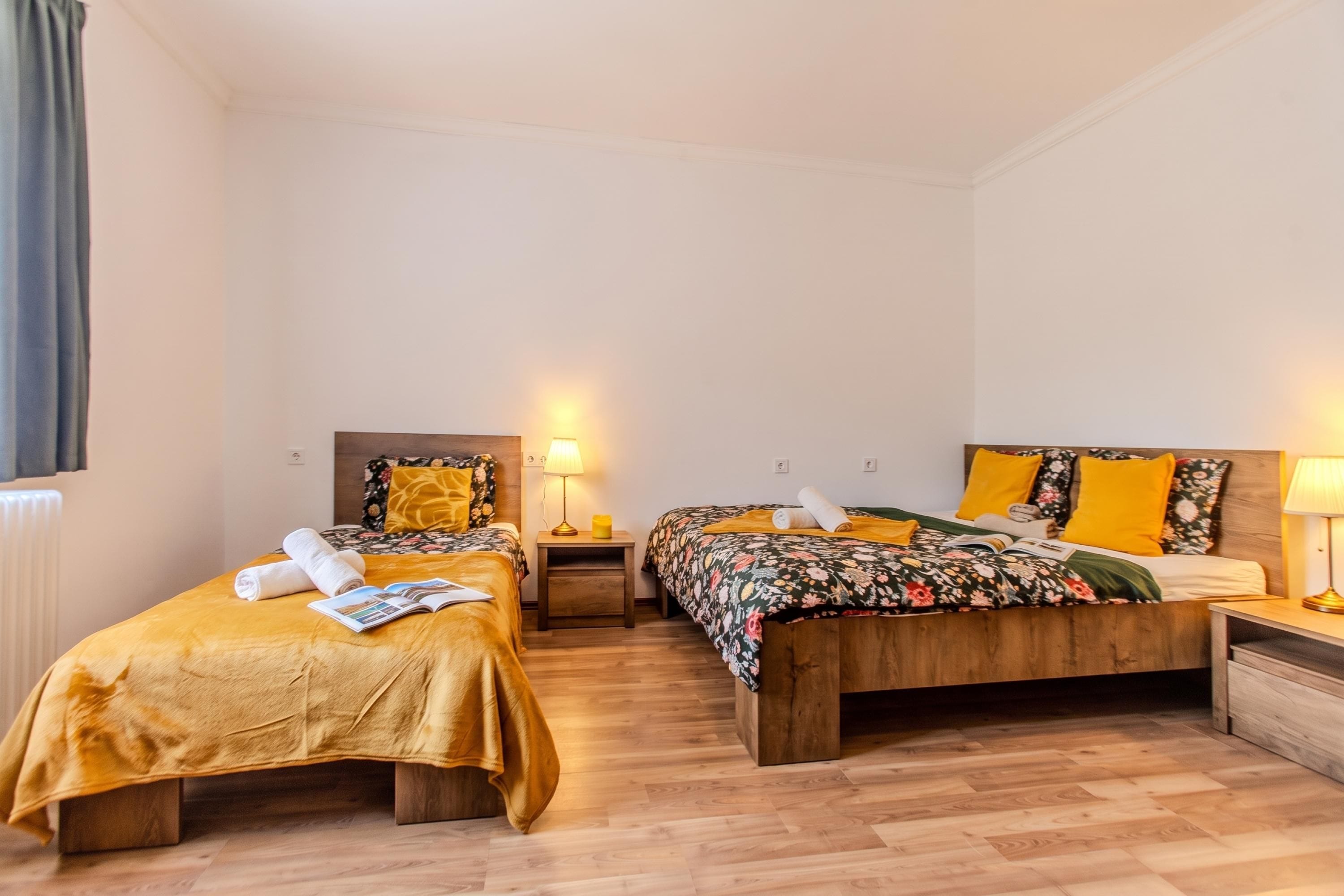 Habitación de hotel con dos camas, suelo de madera y una mesita de noche con lámpara.