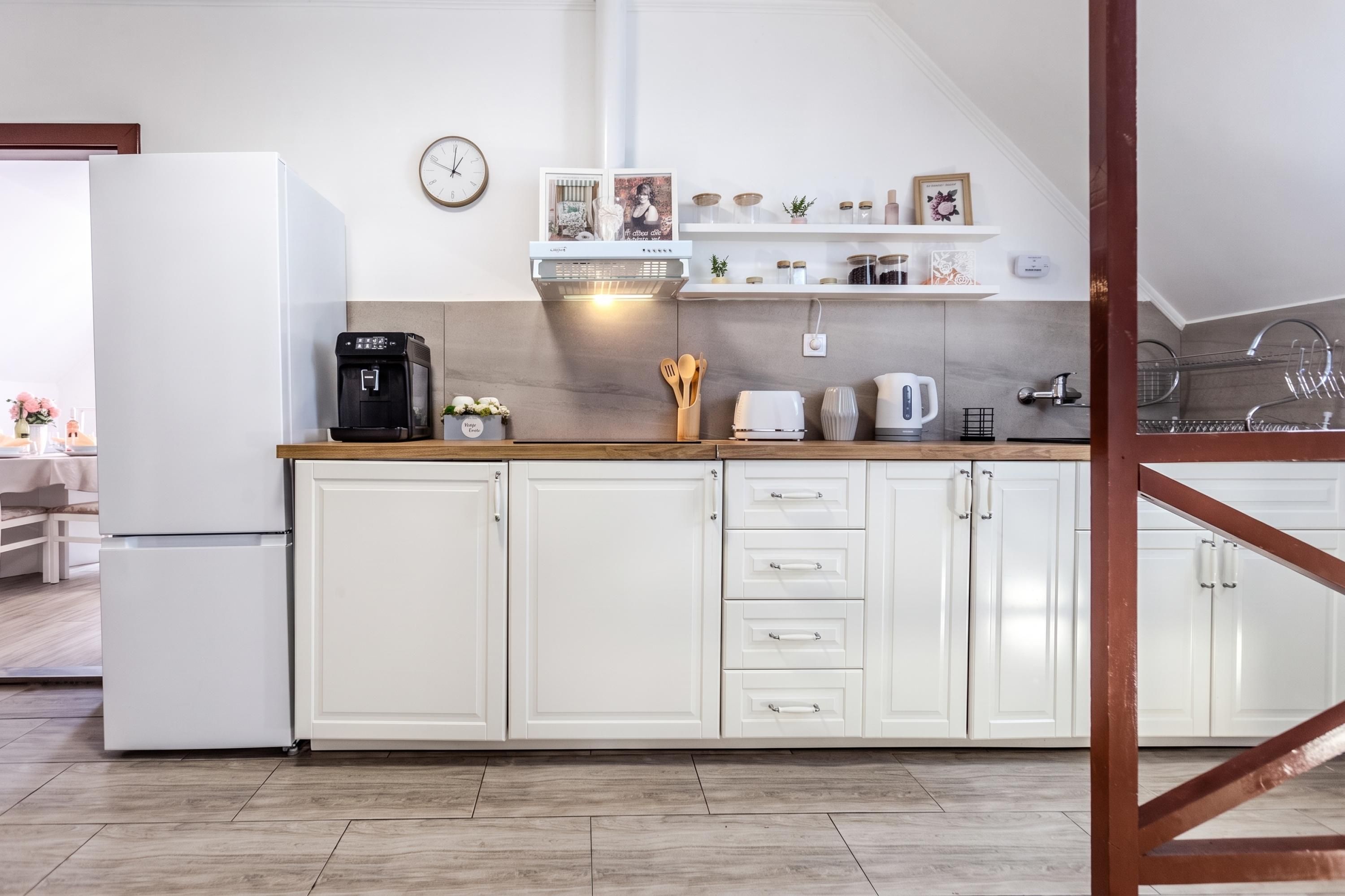 A modern kitchen with white cabinets, a coffee machine, a kettle, and a clock on the wall.