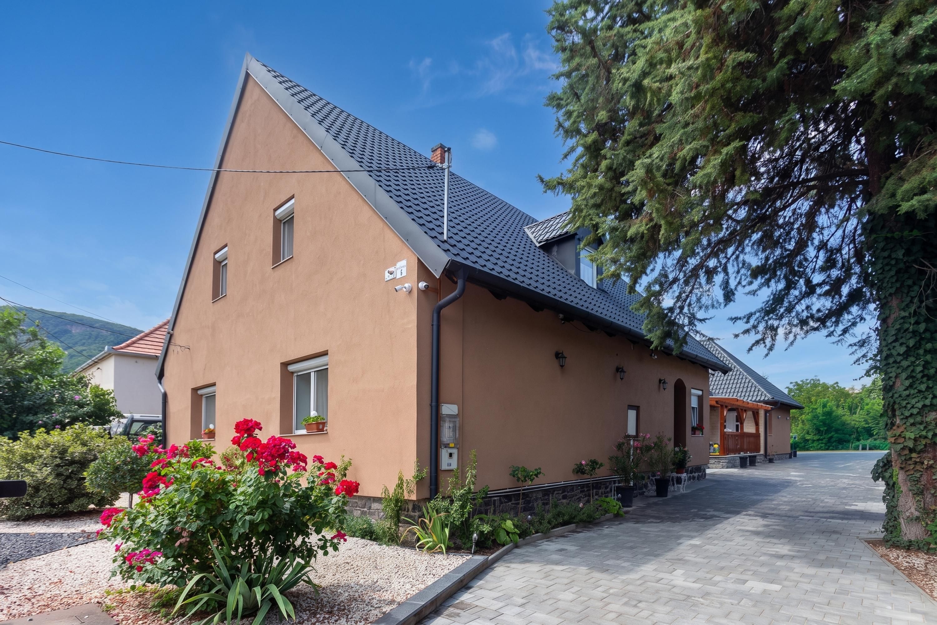 A two-story building with a sloped roof, a paved driveway, and a garden with red flowers.
