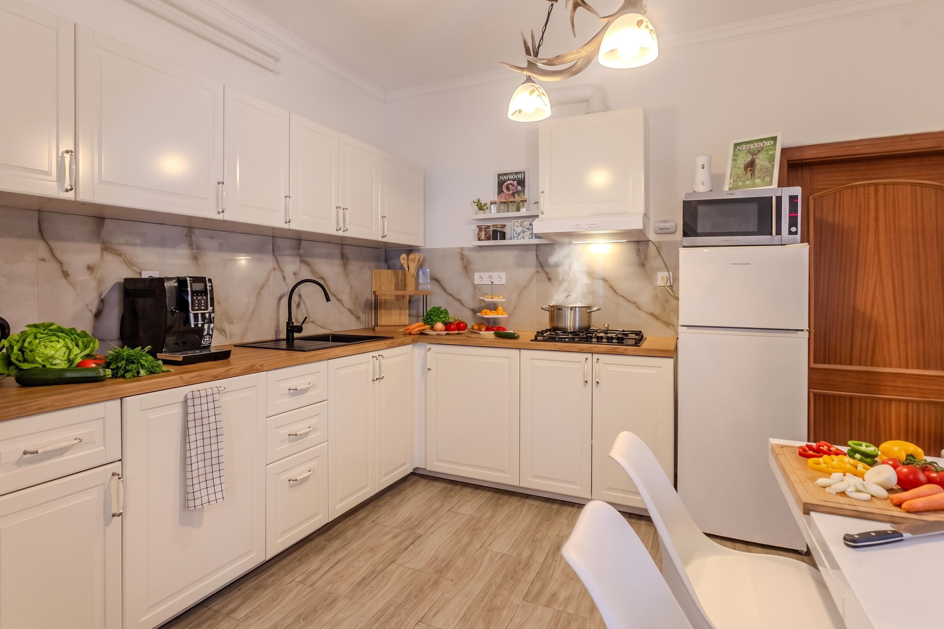 A modern kitchen with white cabinets, a marble countertop, a stove, a microwave, and a refrigerator.