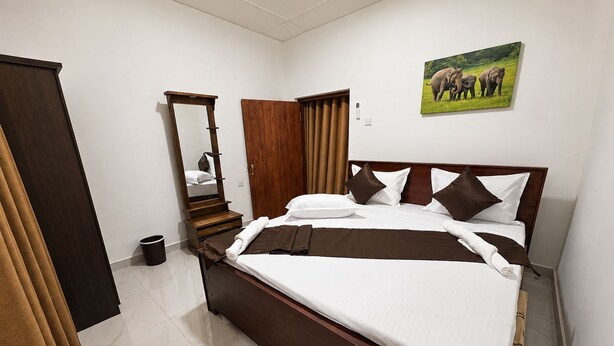 A hotel room with a wooden bed, a large mirror, a picture of elephants, and a wooden wardrobe.