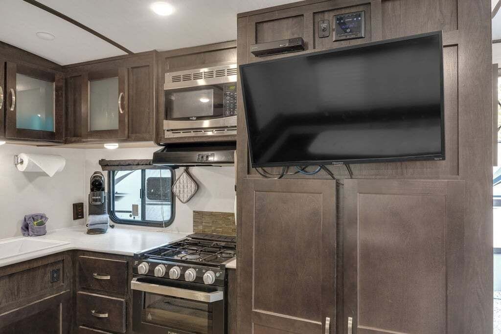 A compact RV kitchen with a stove, microwave, and a flat-screen TV mounted on a cabinet.