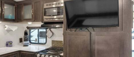 A compact RV kitchen with a stove, microwave, and a flat-screen TV mounted on a cabinet.