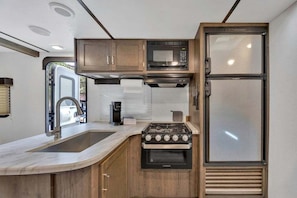 A compact kitchen with a stove, microwave, and refrigerator. - RV Rental D22 - Keystone Passport 32ft (Madras)