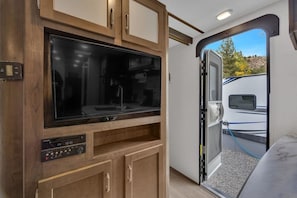 A compact RV interior with a built-in TV, a control panel, and a door leading to an outdoor area. - RV Rental D22 - Keystone Passport 32ft (Madras)
