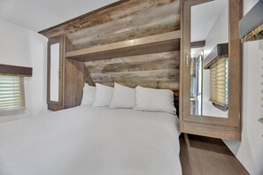 A bedroom with a large bed, wooden headboard, and a mirror. - RV Rental D22 - Keystone Passport 32ft (Madras)