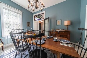 Uma sala de jantar com uma mesa de madeira posta para quatro pessoas, rodeada por cadeiras pretas.