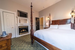 Habitación de hotel con una cama grande, una chimenea, cabecera de madera y una puerta que da a otra habitación.